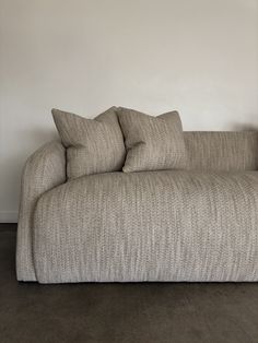 a couch with two pillows on top of it in front of a wall and floor