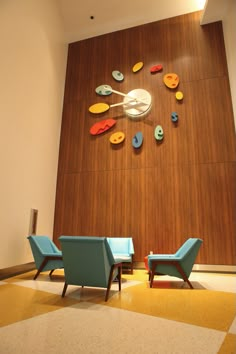 two blue chairs sitting in front of a wall with clocks on it's sides