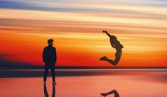 two people are silhouetted against the sunset and one person is jumping in the air