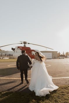 a bride and groom walking towards a helicopter