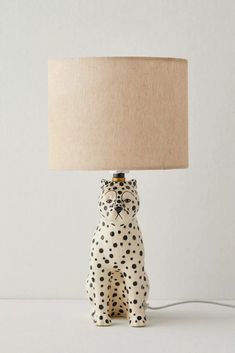 a white and black spotted cat lamp with a beige shade on it's face