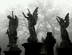 three statues with angel wings on top of headstones in front of some trees