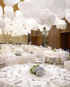 tables and chairs are set up for a wedding reception with white paper lanterns hanging from the ceiling