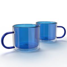 two blue glass mugs sitting next to each other on a white surface with no one around them