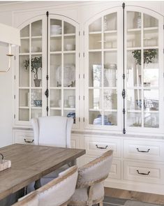 a white china cabinet with glass doors and wooden table in the center, surrounded by chairs