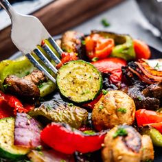 a fork is stuck into a plate of grilled veggies and meats