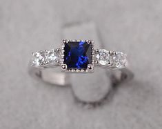 an engagement ring with a blue sapphire surrounded by white diamonds on a gray sand background