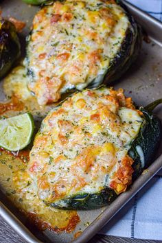 two stuffed peppers on a baking sheet with lime wedges