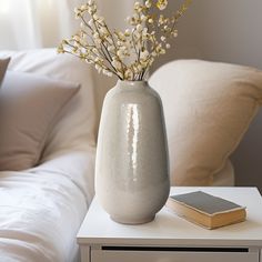 a white vase with some flowers in it sitting on a table next to a book