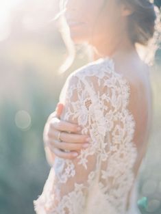 the back of a woman's wedding dress with lace on it and her hand in her pocket