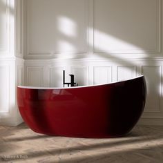 a red bathtub sitting on top of a wooden floor next to a white wall