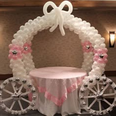 a balloon arch decorated with pink and white balloons on a table in front of a wall