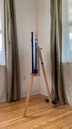 an easel stands in front of two windows with drapes on the window sill