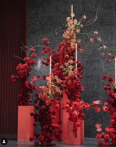 red vases with flowers and candles in front of a wall