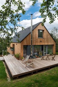 a wooden deck in front of a house with two chairs on it and a fire place