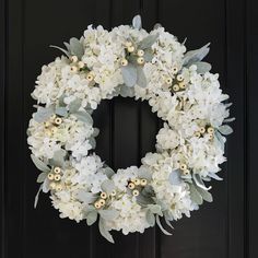 a wreath with white flowers and greenery hangs on a black front door in the daytime