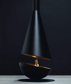 a black vase with a fire in it on top of a white table next to a dark wall