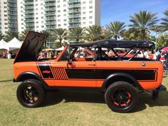 an orange and black truck with its hood open on display at a car show in front of palm trees