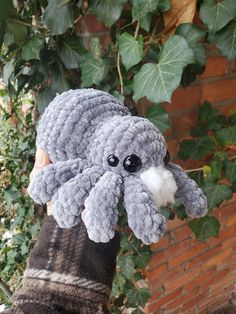 a hand holding up a gray stuffed animal with big eyes and an octopus like head