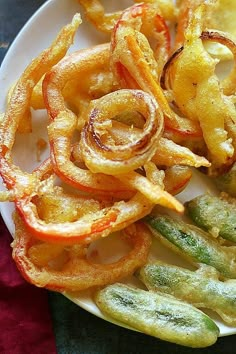 some fried food on a white plate with pickles and onions next to it,