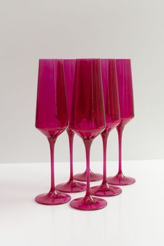 four pink wine glasses are lined up on a white surface, with one empty glass in the middle