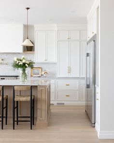 a kitchen with white cabinets and counter tops, two stools in front of the island