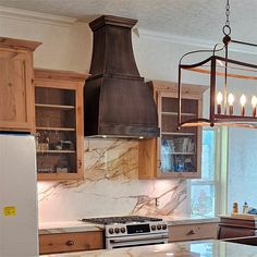 a kitchen with marble counter tops and wooden cabinets, an island style stove hood over the range