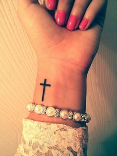 a woman's wrist with a cross tattoo on it and pearls around the wrist