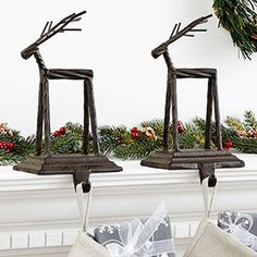 two christmas stockings hanging from hooks in front of a mantel decorated with holly and reindeer antlers