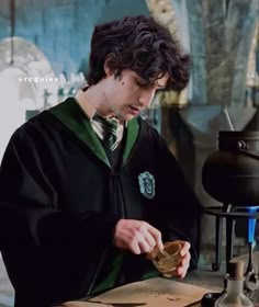 a young man in a harry potter costume is pouring something into a glass jar while sitting at a table