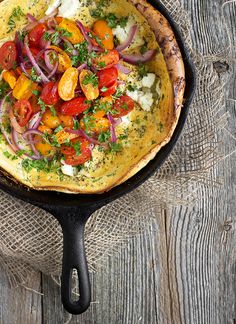 an omelet with tomatoes, onions and herbs in a cast iron skillet