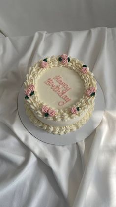 a white cake with pink flowers on it sitting on top of a table covered in white cloth