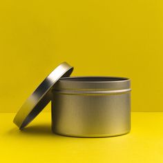 two tins sitting next to each other on a yellow surface with one open and the other closed