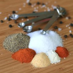 several different types of spices on a wooden table with spoons and seasoning flakes