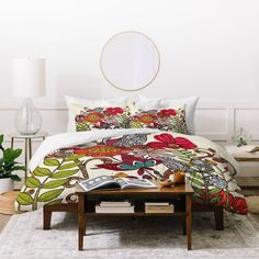 a bed with floral comforter and pillows in a white room next to a coffee table