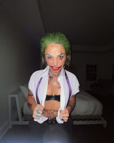 a woman with green hair and piercings on her chest posing for a photo in front of a bed