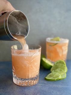 a person pours a drink from a pitcher into a glass with lime slices on the side