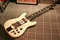 a white electric guitar sitting on top of a tile floor next to a sign that says fine musical instruments