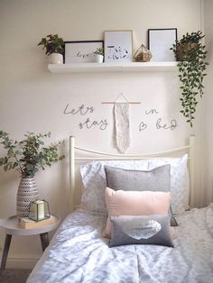 a white bed topped with lots of pillows next to a shelf filled with potted plants