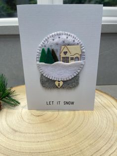 a white card with a house and trees on it that says, let it snow