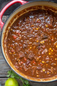 a pot filled with chili and meat on top of a wooden table next to limes