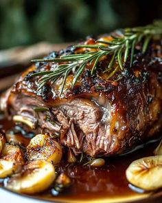 a piece of meat on a plate with potatoes and rosemary sprigs in sauce