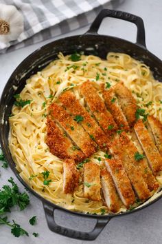 chicken parmesan pasta in a skillet with parsley on the side and garlic sprigs