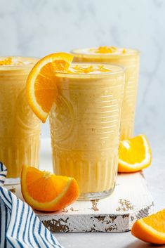 three glasses filled with orange juice and garnished with an orange slice on the side