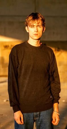 a young man standing in front of a building with his hands in his pockets and looking at the camera