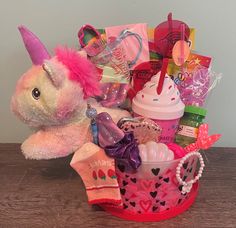 a pink stuffed animal sitting in a basket filled with toys and other items on top of a wooden table