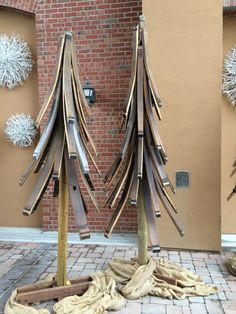 two wooden christmas trees on display in front of a brick building with snowflakes