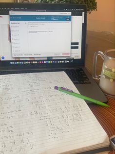 a laptop computer sitting on top of a wooden desk next to a cup and pen