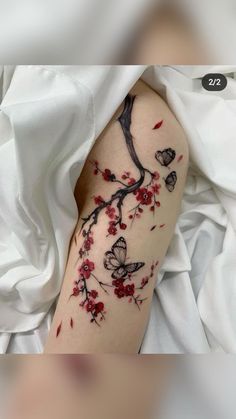 a woman's arm with red flowers and butterflies on it, while she is laying in bed