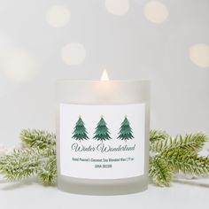 a white candle sitting on top of a table next to evergreen branches and snowflakes